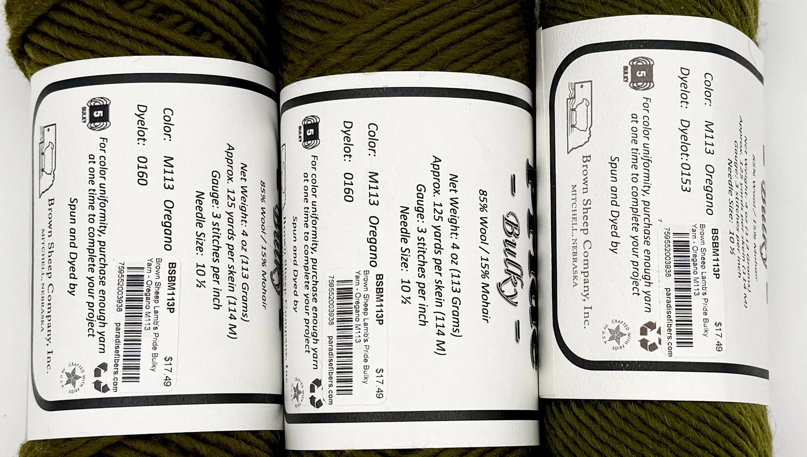 A close-up of a yarn skein label showing the color name and a printed dye lot number, held in someone’s hands under soft indoor light