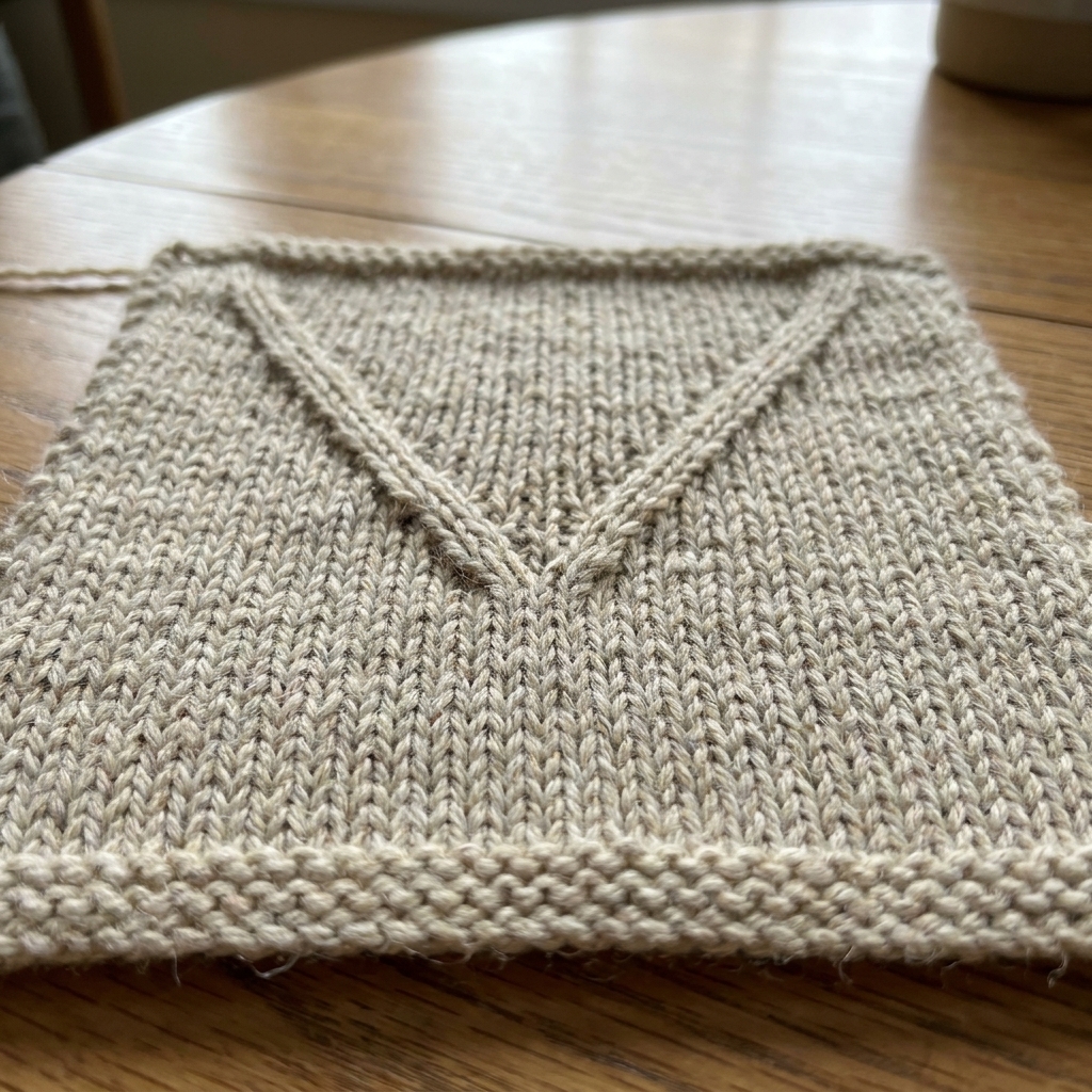 A knitted stockinette swatch laid flat showing two decrease lines that angle inward toward the center