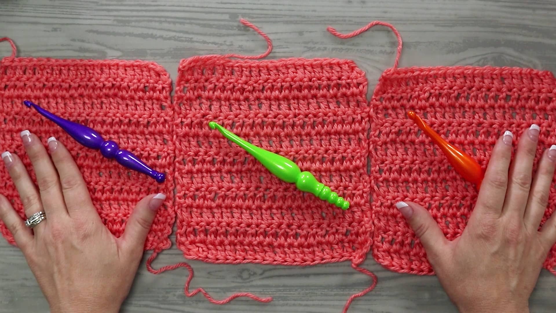 A small rectangular crochet swatch resting on a wooden table beside a crochet hook and a ball of yarn